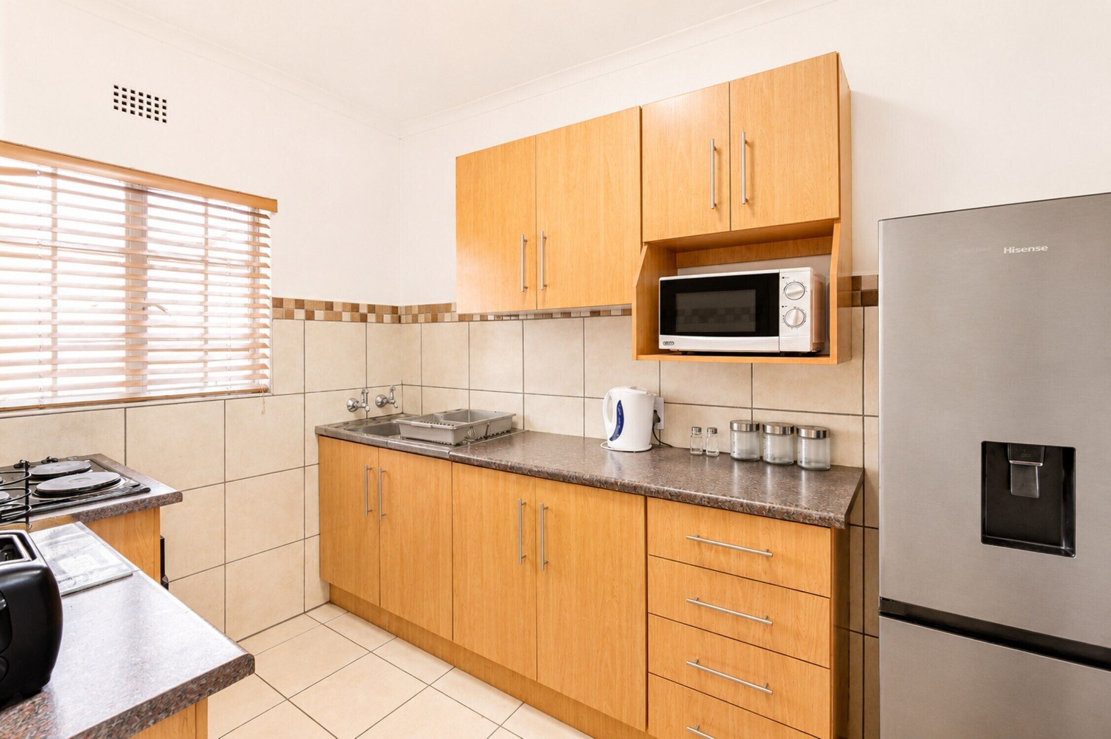 A kitchen with wooden cabinets, a stainless steel refrigerator, a microwave, and a sink.