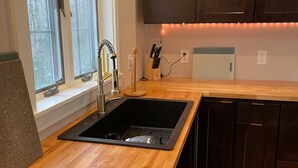 A modern kitchen with a wooden countertop, black sink, and dark cabinets.
