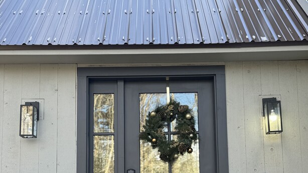 A house with a dark grey front door, a wooden porch, and a metal roof.