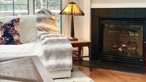 A cozy living room with a fireplace, a sofa with a throw blanket, and a table with a lamp.