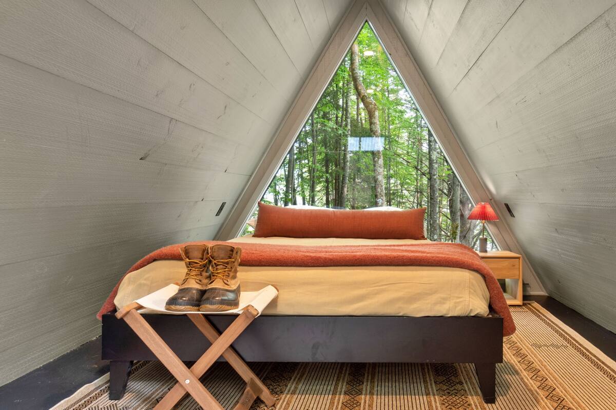 A triangular tent-style room with a bed, a small table, and a red lamp.