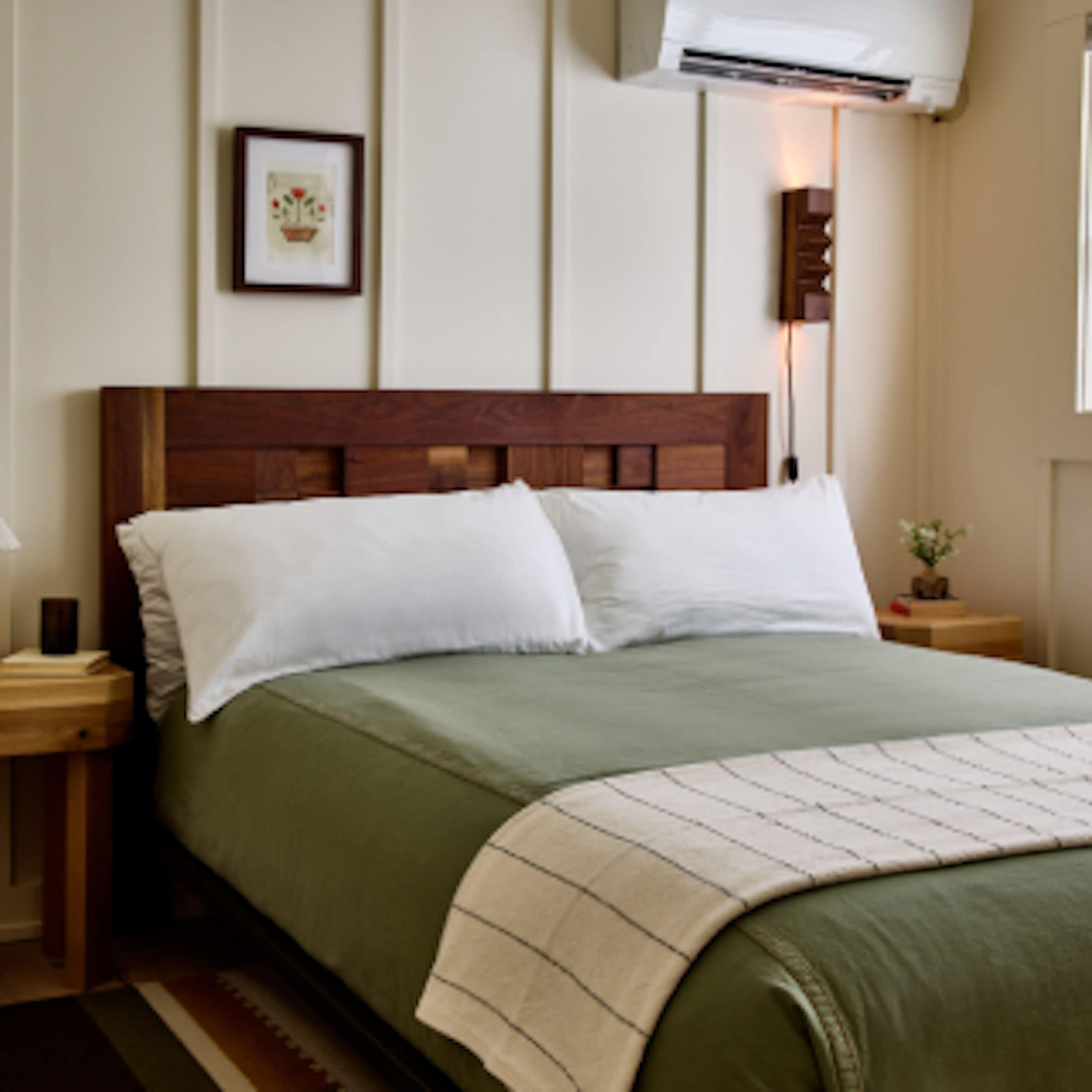 Una cama bien hecha con cabecera de madera, una mesita de noche con lámpara y un cuadro enmarcado en la pared.