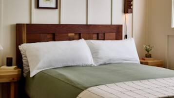 Una cama bien hecha con cabecera de madera, una mesita de noche con lámpara y un cuadro enmarcado en la pared.
