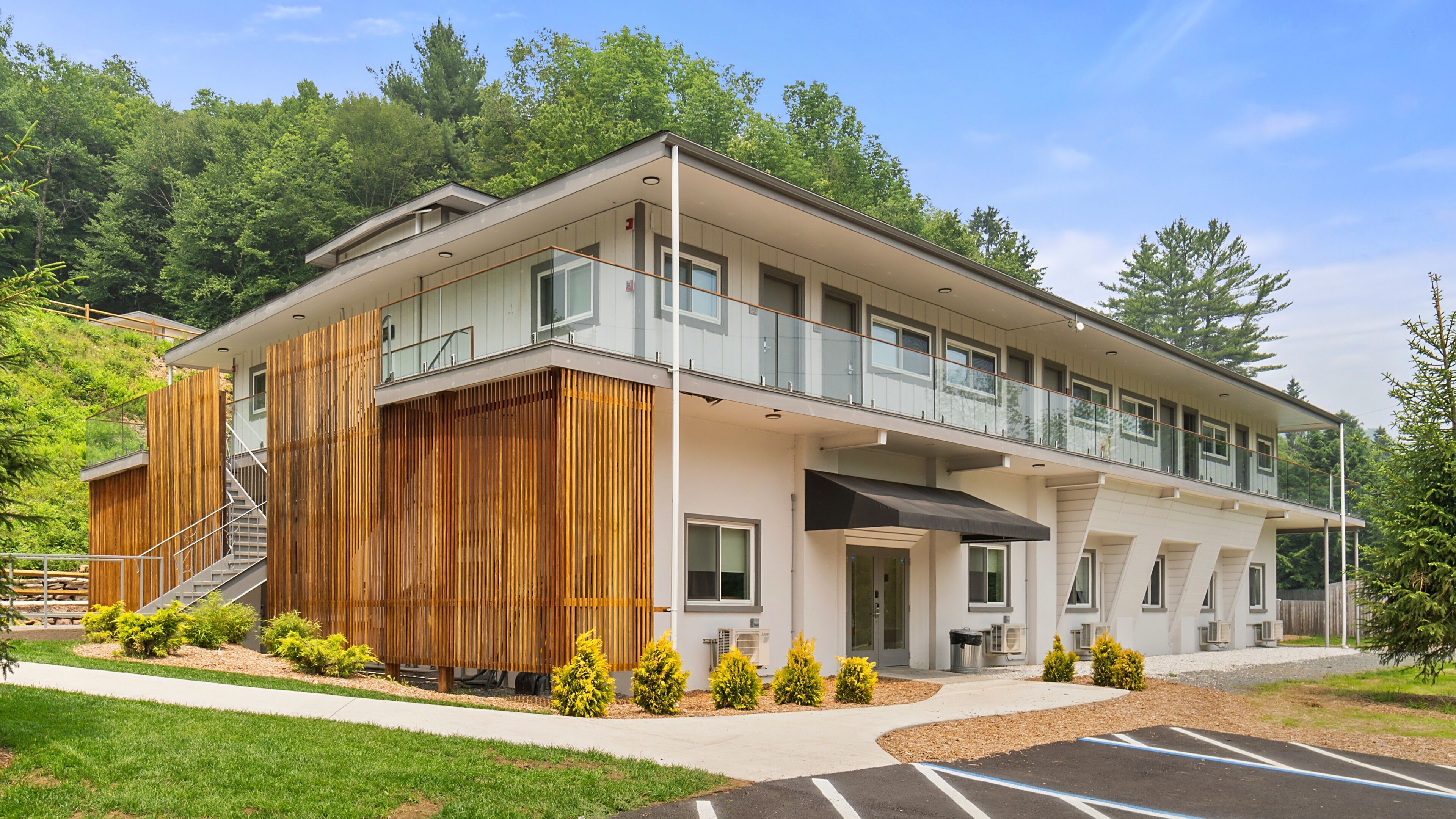 A modern two-story building with a balcony, a staircase, and a parking area.