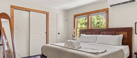 A bedroom with a bed, a wooden headboard, a window with a view of trees, and a door with a geometric design.
