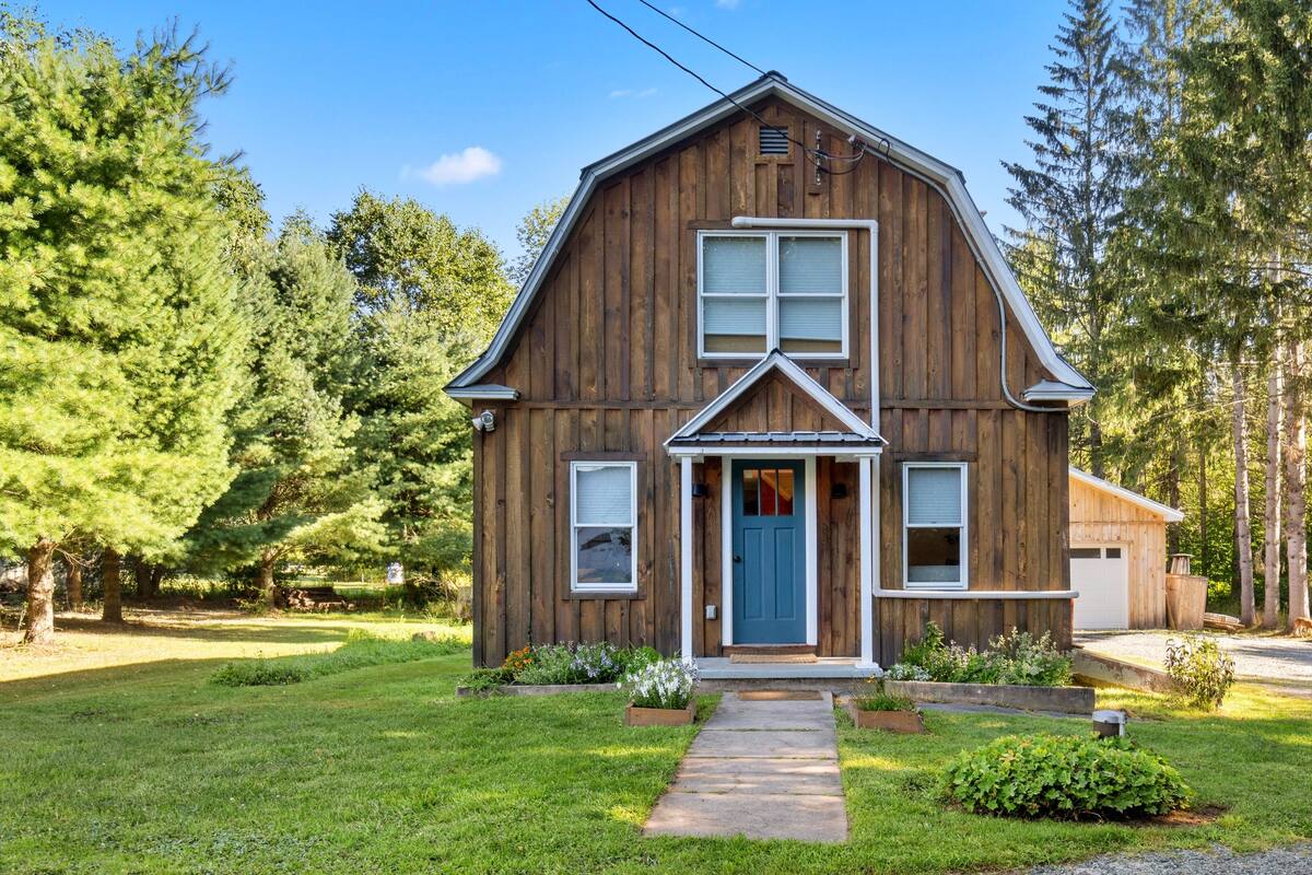 A wooden house with a front porch, a garage, and a well-maintained lawn.