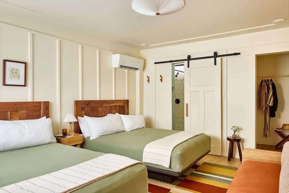A hotel room with two beds, a wardrobe, a small table with a lamp, and a coat rack.