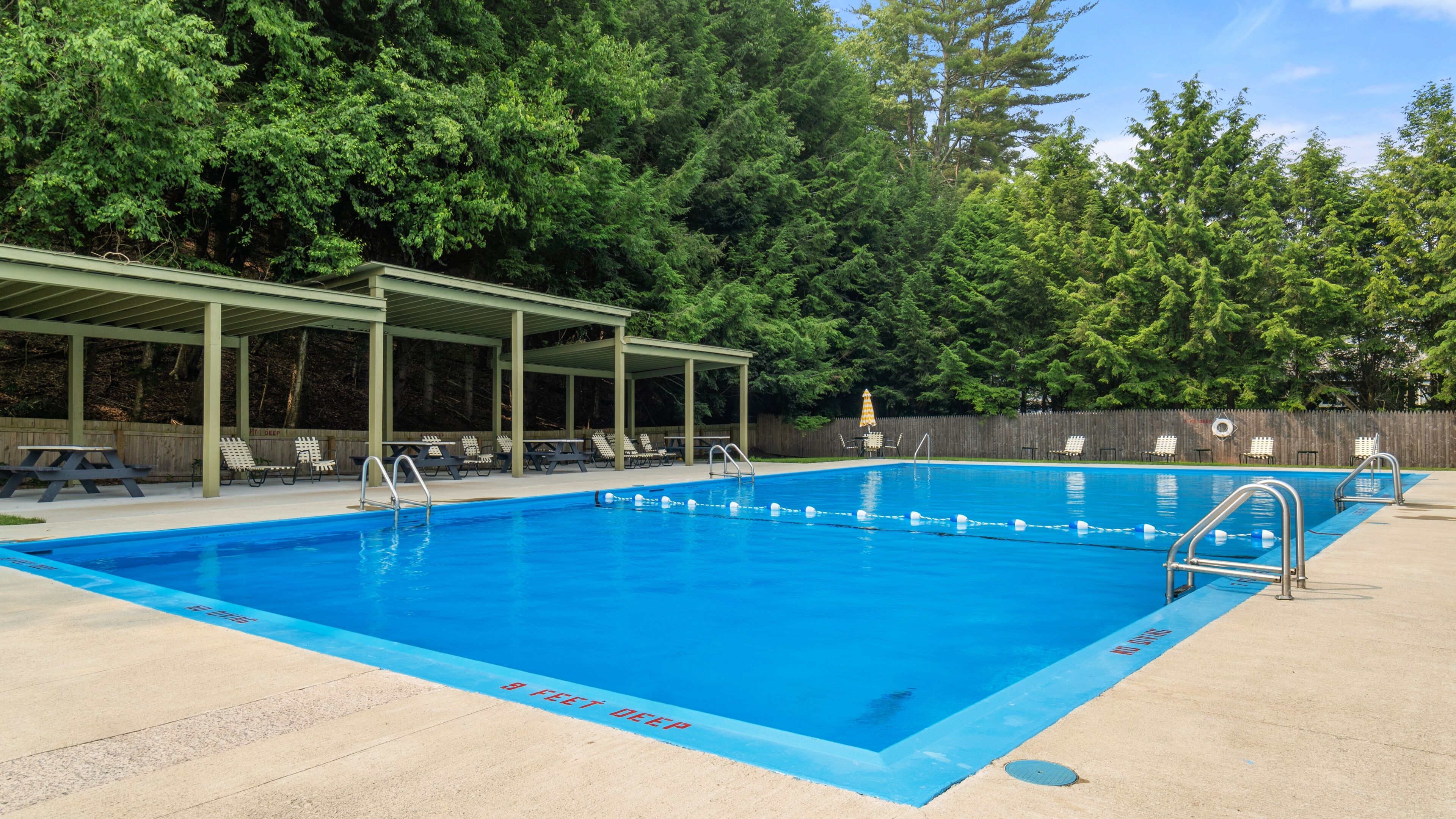 A rectangular swimming pool with a shaded deck area, surrounded by trees.