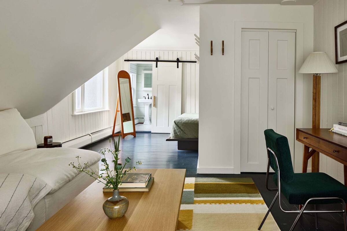 A bedroom with a bed, a desk, a chair, a mirror, and a view of a bathroom.