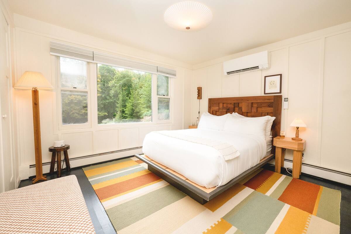 A bedroom with a bed, a window, a bedside table, and a floor lamp.