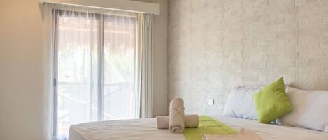 A hotel room with a bed, a green throw blanket, and a window with sheer curtains.