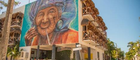 A building with a mural of an elderly person, a balcony with thatched roofs, and a sign that reads "Magalu."