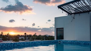 A swimming pool with a sunset view, a modern building with a covered patio, and a clear sky with clouds. - Hotel Mayari Holbox (Isla Holbox)