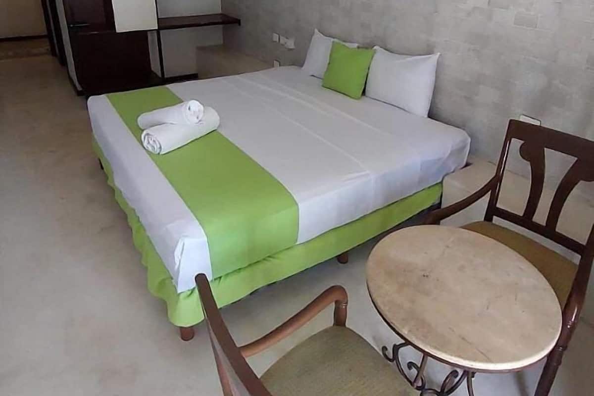 Ein Hotelzimmer mit Bett, Sessel, kleinem Tisch und Deckenventilator.