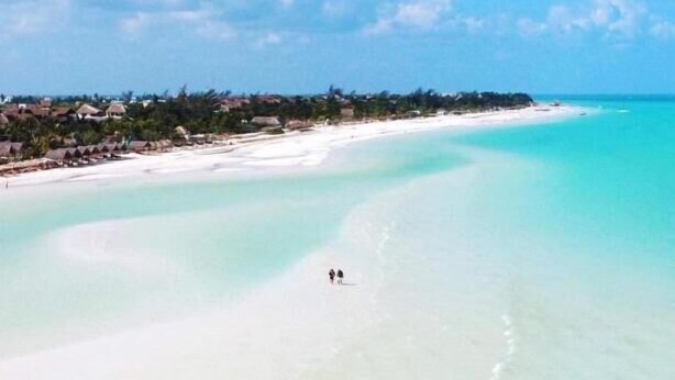 An aerial view of a beach with clear turquoise waters and a few people walking along the shore. - Hotel Mayari Holbox (Isla Holbox)