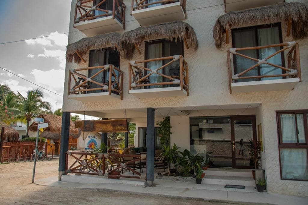 Ένα διώροφο κτίριο με μπαλκόνια που διαθέτουν στέγες από καλάμια, έναν σκεπαστό εξωτερικό χώρο με καθίσματα και μια πινακίδα που υποδεικνύει ότι πρόκειται για ένα ξενώνα.