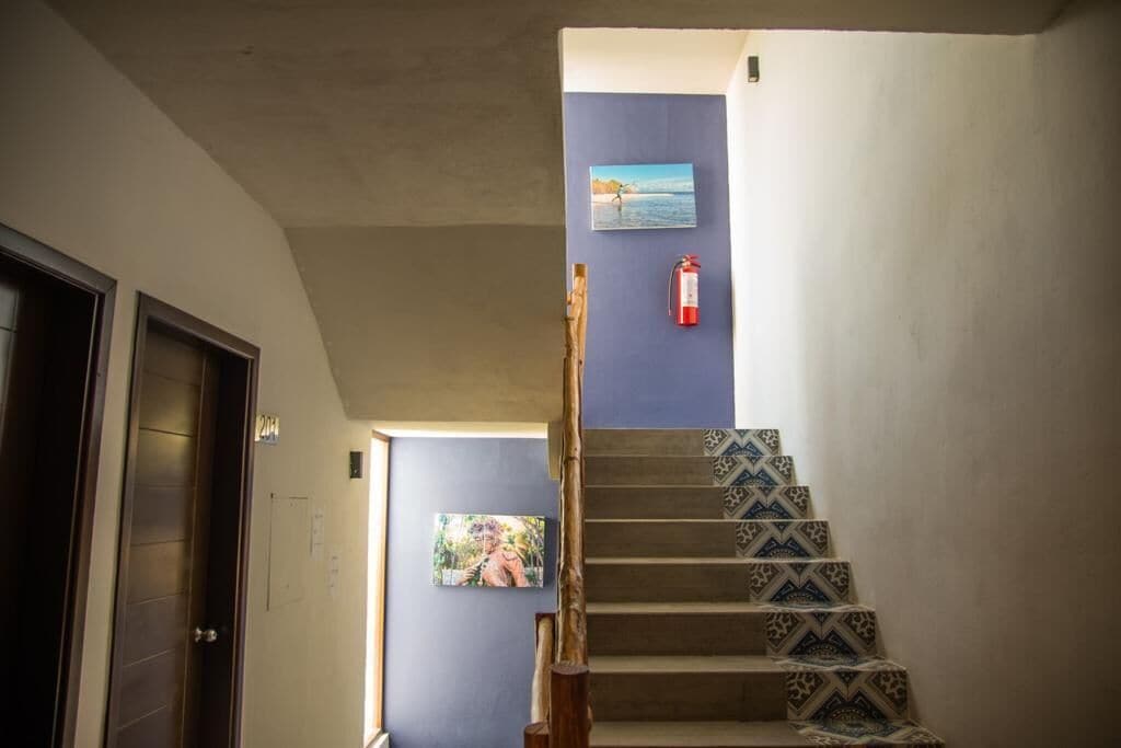 Una escalera con baldosas estampadas, un extintor de incendios fijado a la pared y dos cuadros enmarcados.