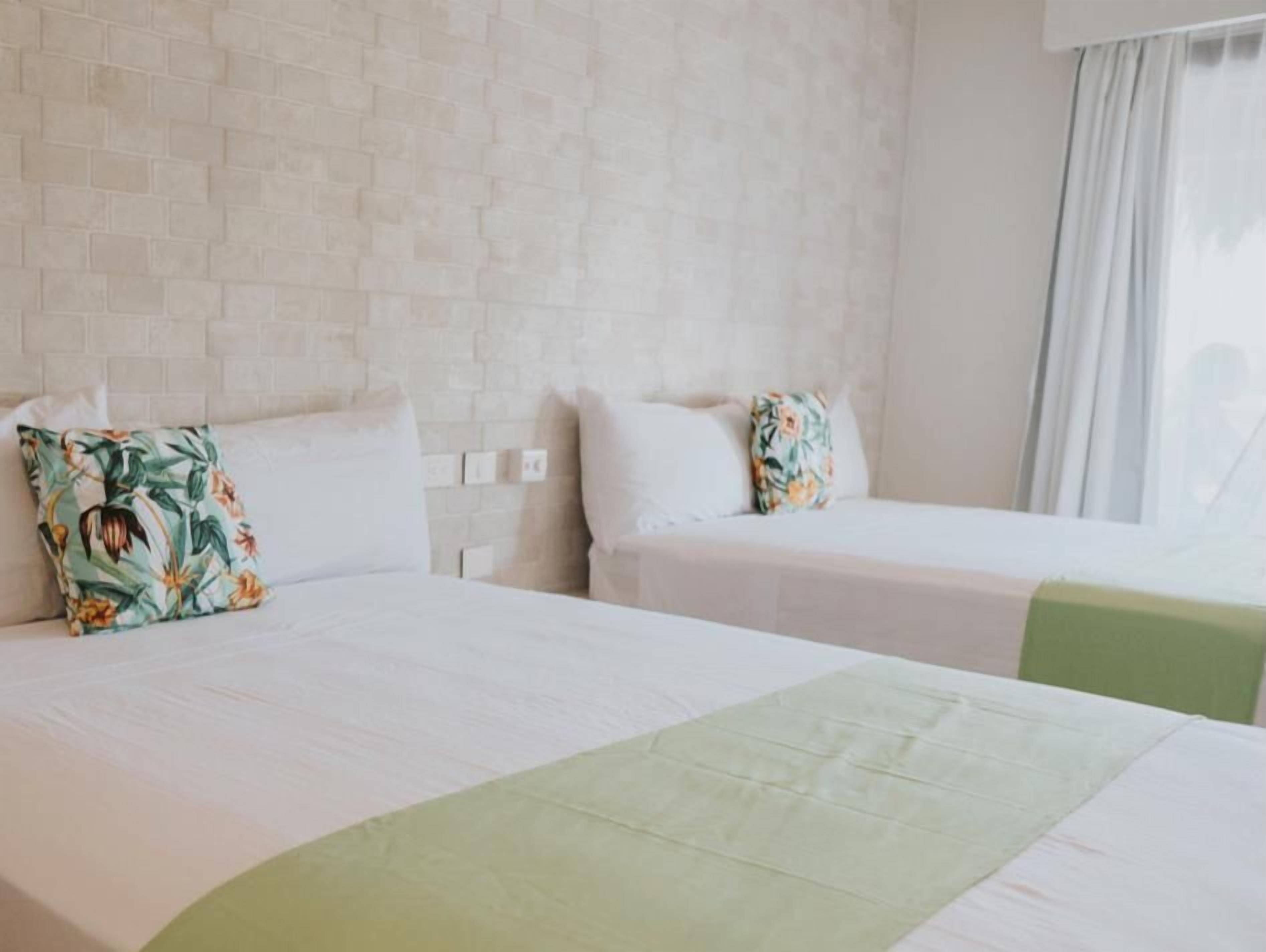 A hotel room with two beds, a brick-patterned wall, and a window with curtains.