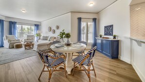 A spacious living area with a round dining table, blue and white striped chairs, a white sofa, and a blue cabinet. - Private Balcony Overlooking Pool & Ocean (Hilton Head Island)