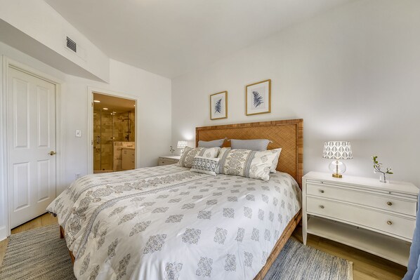 Une chambre à coucher avec un grand lit, une table de chevet, une commode et une porte donnant sur une salle de bain.