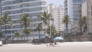 Ein Strand mit Palmen, einem blau gestreiften Sonnenschirm und einer Person, die sich sonnt.