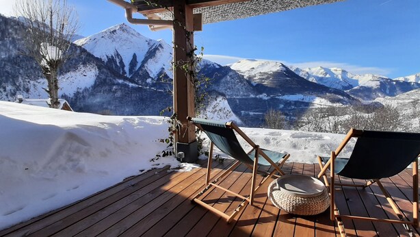 Una terraza de madera con dos sillas y una cesta tejida, con vistas a un paisaje montañoso nevado.