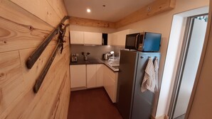 Una cocina compacta con paredes de madera, un refrigerador de acero inoxidable, un microondas y un lavamanos.