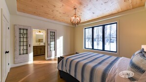 Een slaapkamer met een groot raam, houten vloer en een bed met een gestreept dekbed.