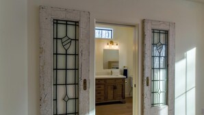Een gang die leidt naar een badkamer met een houten wastafel en een spiegel erboven.