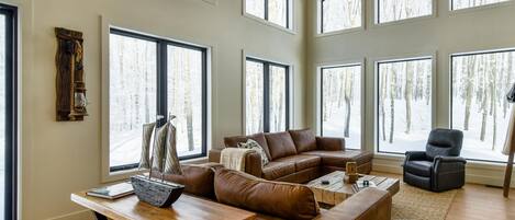 A spacious living room with large windows, a wooden ceiling, and a fireplace.