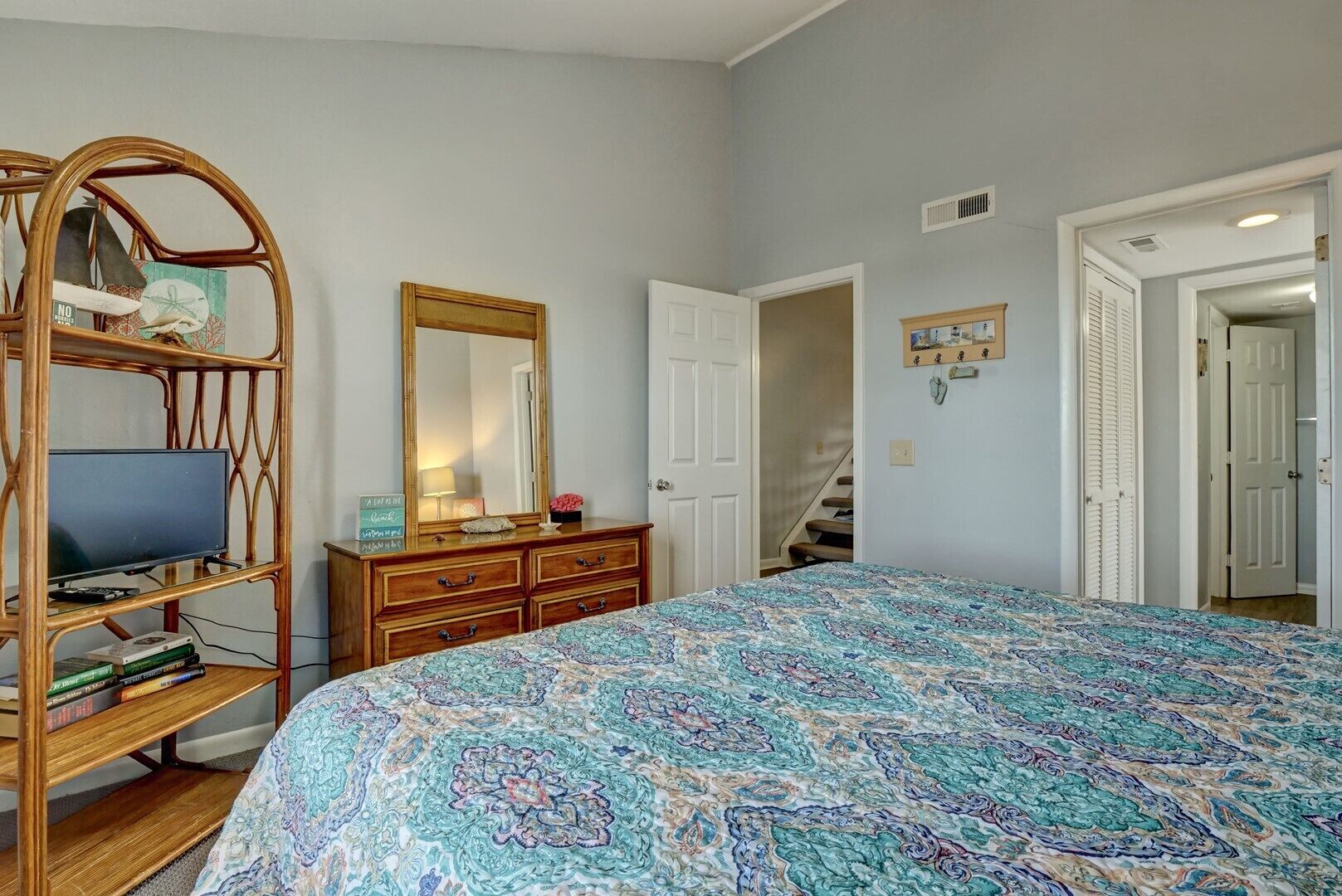 A bedroom with a large bed, a wooden dresser, a television on a stand, and a mirror.