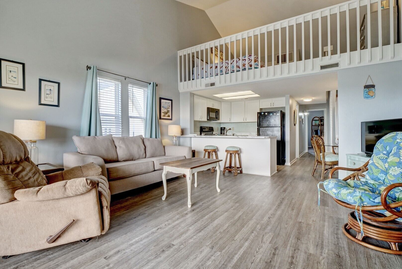 A spacious living room with a high ceiling, a dining area, and a kitchen with a central island.