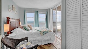 A bedroom with a large bed, a wicker chair, and a view of the ocean through large windows. - Top floor, oceanfront views! (North Topsail Beach)