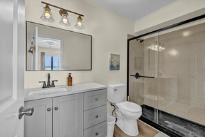 Ein modernes Badezimmer mit einem großen Spiegel, einem weißen Waschbecken, einer Toilette und einer Duschkabine.