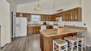 Eine moderne Küche mit Holzschränken, einer zentralen Kochinsel mit Barhocker, einem Kühlschrank, einer Mikrowelle und einer Kaffeemaschine.