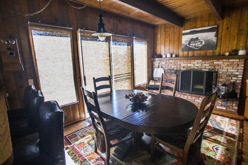 A rustic dining area with a wooden table, chairs, and a brick fireplace.