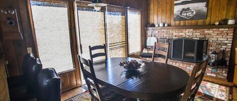 A rustic dining area with a wooden table, chairs, and a brick fireplace.