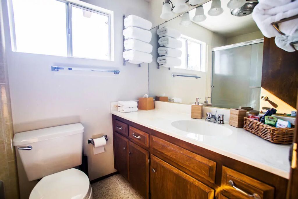 Une salle de bain avec des toilettes, un lavabo, des meubles en bois, un miroir et des serviettes accrochées au mur.