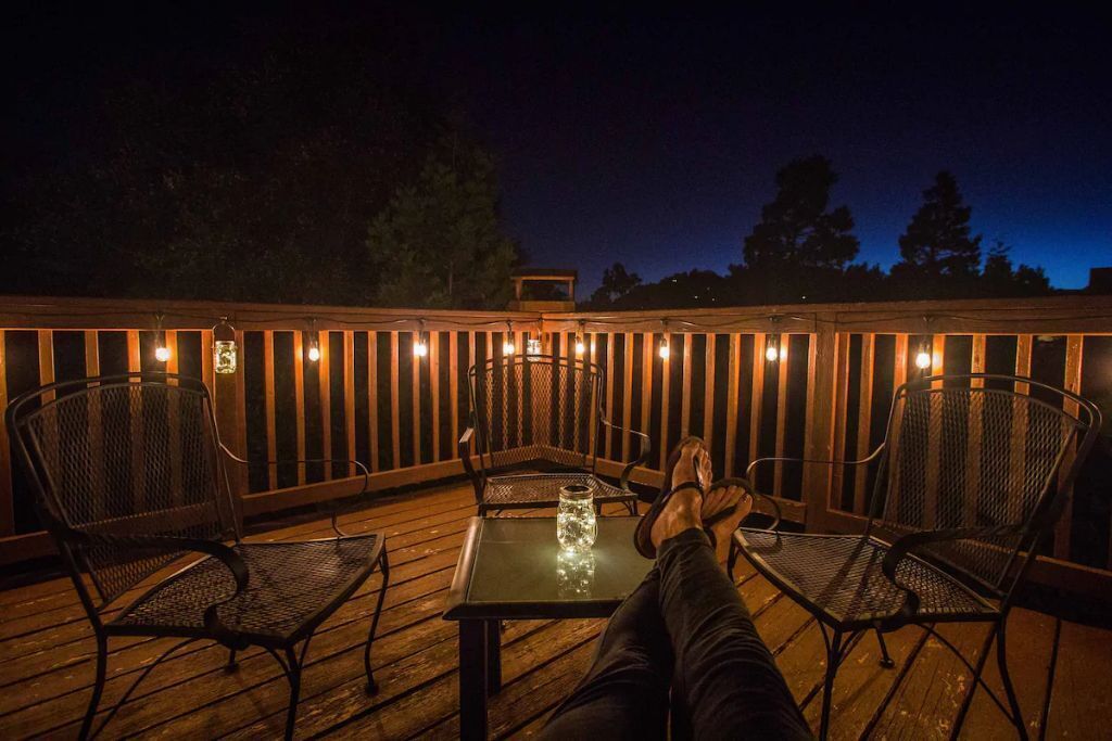 A deck with a table and chairs, surrounded by a wooden railing with lights.