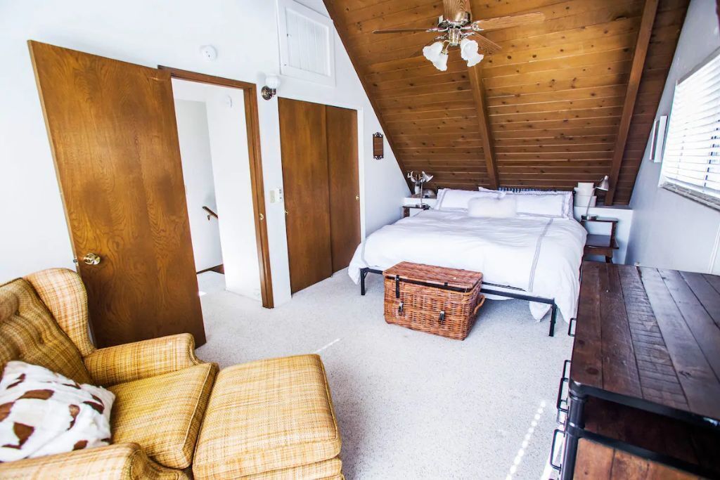 Ein Schlafzimmer mit Holzbalkendecke, einem Bett, einer Korboffle und einem Sessel.