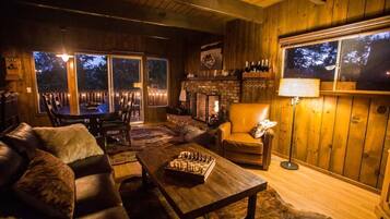 A cozy living room with a fireplace, leather furniture, and a large window overlooking a deck.