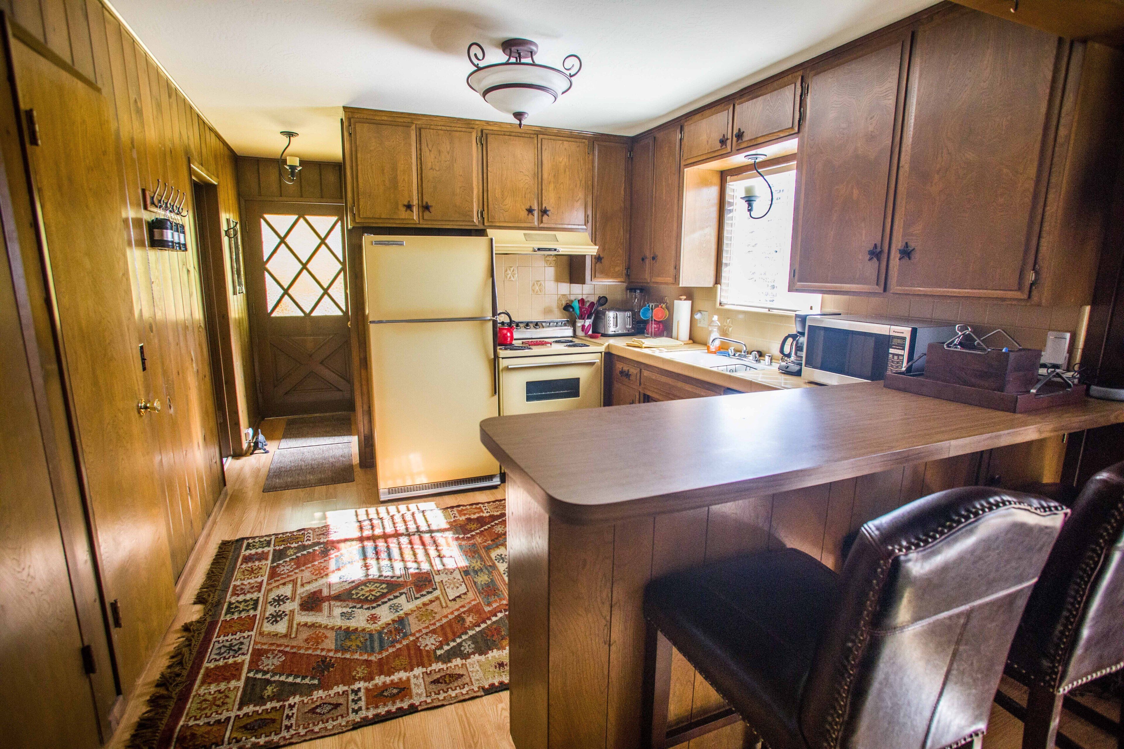 A kitchen with wooden cabinets, a refrigerator, stove, microwave, and a bar area.