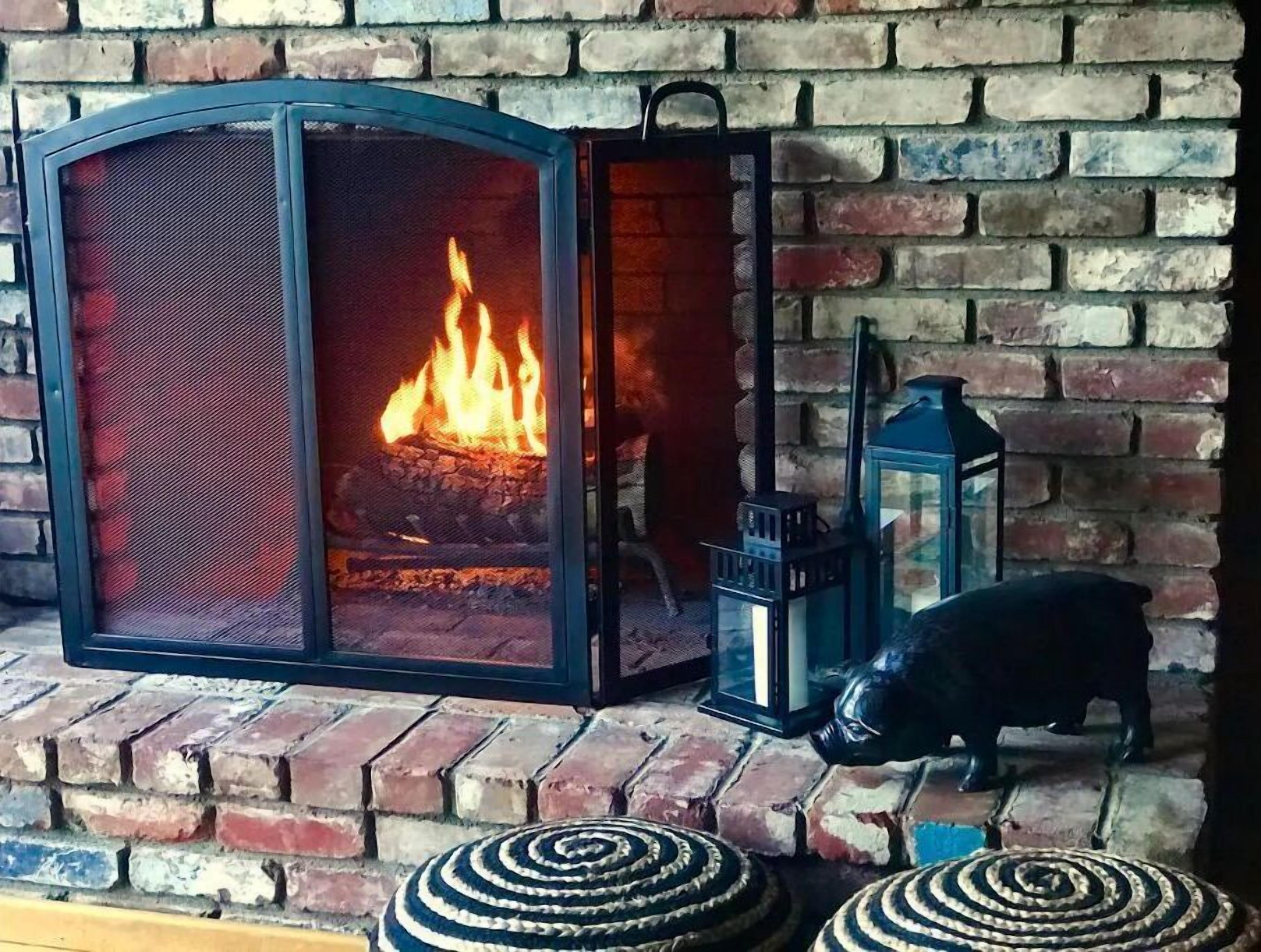 Lareira com fogo, um candeeiro e uma estatueta de porco numa parede de tijolos.