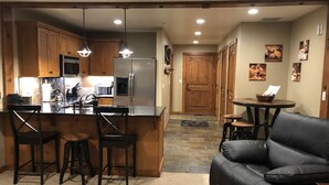 Una cocina moderna con una isla central, taburetes de bar, un sofá de cuero negro y suelo de baldosas de piedra.