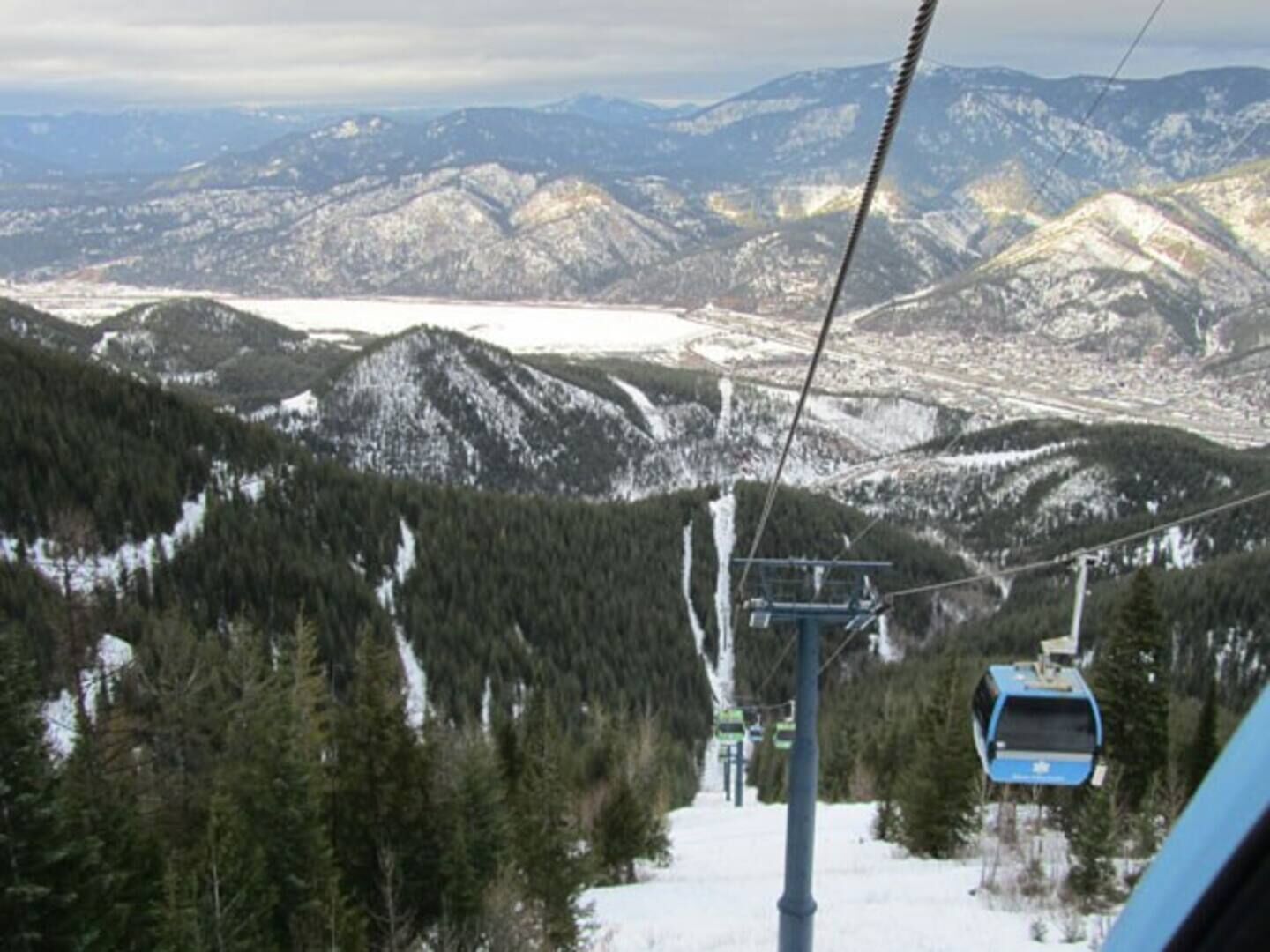 A cable car moving through a mountainous area with snow-covered peaks and dense forests.
