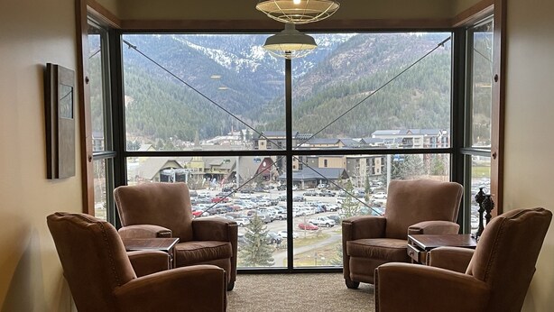 Una habitación con dos sillones de cuero marrón, piso alfombrado y un ventanal con vistas a un estacionamiento y montañas.