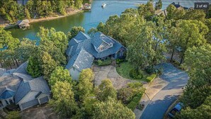 An aerial view of a residential area with multiple houses, a lake, and a dock. - Waterfront 5000 sq. ft. on cove, boat dock & 2 large decks, Media & Game Room. (Hot Springs Village)