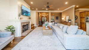 A spacious living room with a fireplace, a large sectional sofa, and a flat-screen TV mounted on the wall. - Waterfront 5000 sq. ft. on cove, boat dock & 2 large decks, Media & Game Room. (Hot Springs Village)