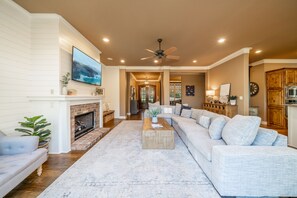 A spacious living room with a fireplace, a large sectional sofa, and a flat-screen TV mounted on the wall. - Waterfront 5000 sq. ft. on cove, boat dock & 2 large decks, Media & Game Room. (Hot Springs Village)