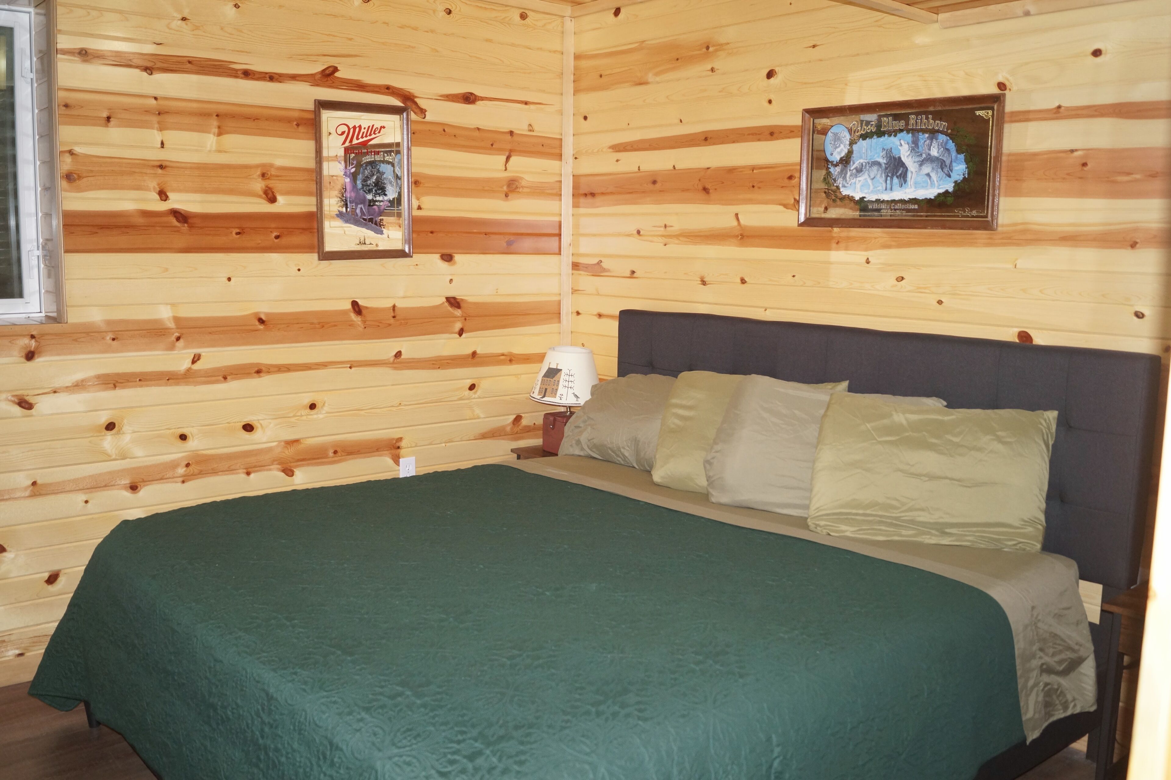 Una habitación de cabaña de madera con una cama, una mesita de noche y dos cuadros en las paredes.